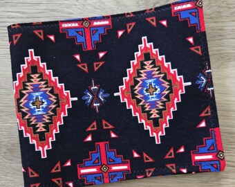 May include: A rectangular fabric wallet featuring a black background with a repeating geometric pattern in red, blue, white, and brown. The design consists of large diamond shapes and cross motifs with intricate stepped edges and stitched borders.