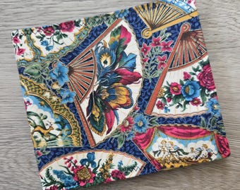 May include: A square fabric item featuring a vibrant, multi-colored pattern of folding fans, floral arrangements, and classical cherub illustrations. The design incorporates deep blue, red, yellow, and green tones with intricate decorative borders.