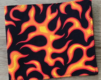 May include: A square fabric piece featuring a repeating flame pattern in vibrant shades of orange, yellow, and red set against a solid black background. The edges of the textile are finished with a visible black zigzag stitch along the perimeter.