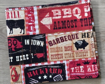 May include: A square fabric napkin featuring a collage of barbecue-themed graphics in red, black, white, and tan. The print includes illustrations of a cow and a pig, along with text such as BBQ, IN TOWN, BACKYARD, and a list of meats like burgers and brisket.