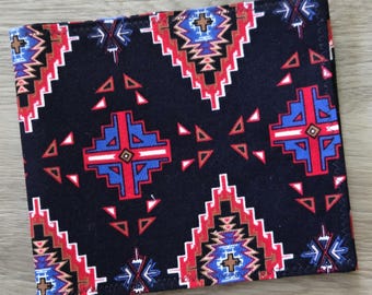 May include: A rectangular fabric item featuring a black background with a repeating geometric pattern in red, blue, white, and brown. The design consists of stepped diamond shapes and smaller triangular accents arranged in a symmetrical layout.