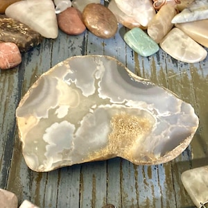 May include: A large, irregularly shaped agate stone with a light gray and brown color pattern. The stone has a smooth, polished surface.