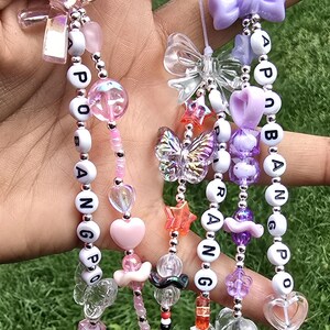 May include: Three beaded phone charms featuring white letter beads spelling POBANGPO and RANG. The charms include pink, purple, and clear plastic beads in shapes of hearts, butterflies, stars, and bows, attached to white string loops for attachment.