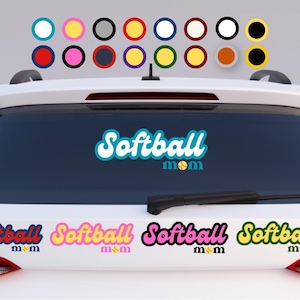Puede incluir: La luneta trasera de un coche blanco muestra una pegatina de color turquesa y blanco con el texto Softball mom, donde la letra o es una pelota de softball amarilla. Debajo, cuatro pegatinas en rojo, rosa, negro y amarillo muestran el mismo texto.