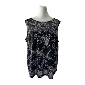 Puede incluir: Una blusa negra sin mangas con una capa de malla transparente con un patrón de puntos blancos. La prenda tiene un cuello redondo y una capa base negra sólida debajo, creando un efecto de capas con una sección superior semitransparente.