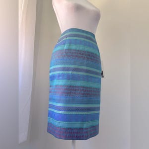 May include: A knee-length skirt with horizontal stripes in shades of blue, teal, and purple. The skirt has a fitted silhouette and a subtle pattern within the stripes. The skirt is displayed on a mannequin.