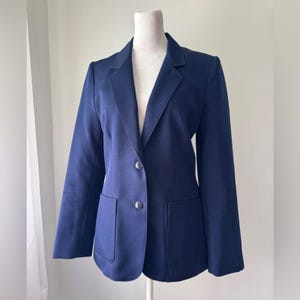 Peut inclure: Un blazer bleu marine au design classique. Le blazer présente un revers cranté, deux poches avant et deux boutons pour la fermeture. Le vêtement est présenté sur un mannequin sur fond blanc.