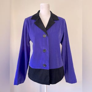 May include: A purple blazer with a black collar and black trim at the bottom. The blazer has three black buttons down the front.