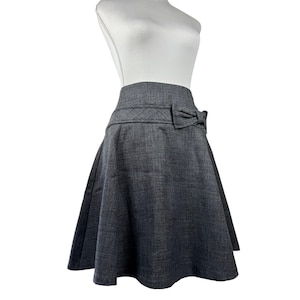 May include: A gray, flared skirt with a bow detail at the waist. The skirt is made of a textured fabric and has a classic, feminine silhouette. The bow is centered on the front of the skirt.