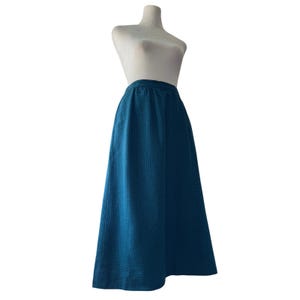 May include: A teal-colored, full-length skirt with a subtle checkered pattern. The skirt is displayed on a mannequin, showcasing its A-line silhouette and elastic waistband. The fabric appears to be a medium-weight material, suitable for various seasons.
