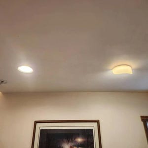 May include: A ceiling with two light fixtures. One is a recessed, circular light, and the other is a curved, surface-mounted fixture. The ceiling and walls are painted a light beige color, and a framed picture is visible below.