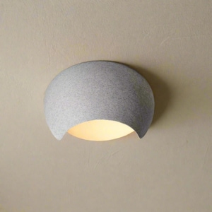 May include: A gray, speckled, semi-circular wall sconce with a warm, yellow glow emanating from the curved opening. The fixture is mounted on a light beige wall, creating a soft, ambient light.