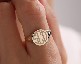 May include: A gold signet ring featuring a circular face engraved with the monogram letters SCD in a classic serif font. The ring has a polished metallic finish and a smooth, tapered band that sits comfortably on the finger.