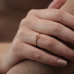 May include: A delicate gold ring with a small pink gemstone set in a square frame.