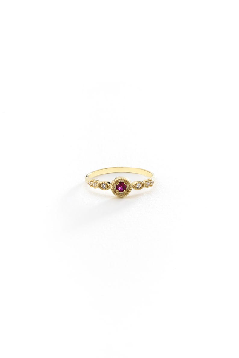 May include: A gold ring featuring a red gemstone surrounded by smaller white gemstones.