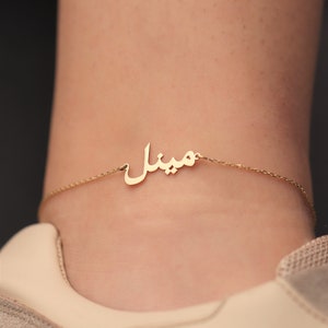 Könnte beinhalten: Ein goldenes Fußkettchen mit dem arabischen Wort "Minal" darauf.