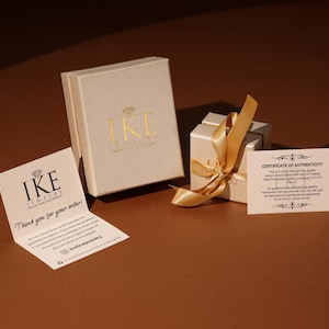 以下が含まれることがあります： 2つのベージュ色の箱、金色のリボンが付いた箱、そして「IKE JEWELRY」と書かれた折り畳まれたカードが特徴のジュエリープレゼンテーション。 鑑定書も付属しています。 箱には金色の「IKE」ロゴが入っています。