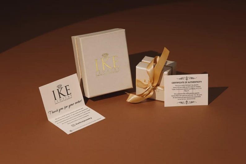 a jewelry box with a gold ribbon, a small white box with a gold ribbon, and a white card with text on a brown background.
