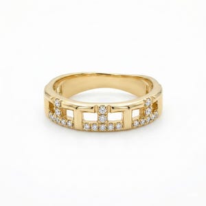 Puede incluir: Un anillo de oro con un dise&ntilde;o geom&eacute;trico. El anillo presenta cortes rectangulares y est&aacute; adornado con peque&ntilde;as gemas brillantes. La banda tiene un acabado liso y pulido, y el dise&ntilde;o es moderno y elegante. El anillo mide aproximadamente 1,5 cm de ancho.