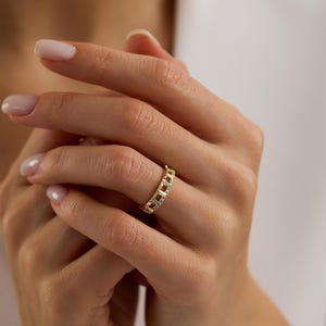 Puede incluir: Un anillo dorado con un dise&ntilde;o de eslabones de cadena, engastado con peque&ntilde;as piedras preciosas transparentes. El anillo se lleva en un dedo, mostrando sus intrincados detalles y acentos brillantes. El dise&ntilde;o del anillo es moderno y elegante.