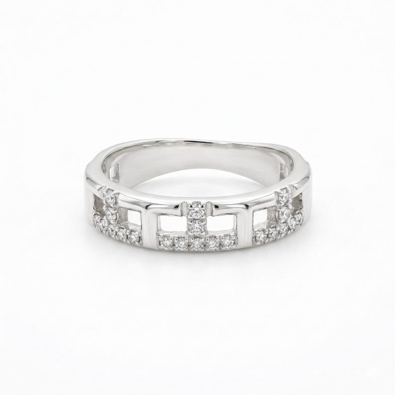 Puede incluir: Un anillo plateado con un dise&ntilde;o geom&eacute;trico. El anillo presenta una serie de cortes rectangulares y est&aacute; incrustado con peque&ntilde;as piedras preciosas brillantes. La banda tiene un acabado liso y pulido, creando un aspecto moderno y elegante.