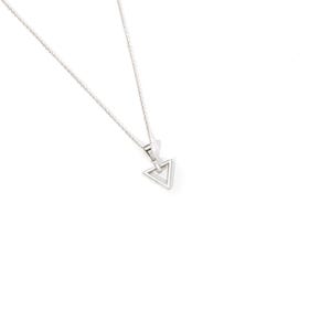 Puede incluir: Collar plateado con un colgante triangular hueco. El colgante cuelga de una cadena fina. El collar se muestra sobre un fondo blanco.