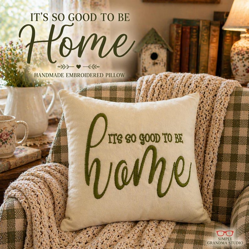 Cream mini pillow embroidered with It’s so good to be Home in green, resting on an armchair with a knitted throw