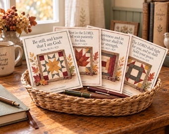 May include: A woven wicker basket containing four rectangular cards featuring autumn-themed quilt block illustrations and Bible verses. The cards display text including Be still, and know that I am God, Rest in the LORD, and wait patiently for him.