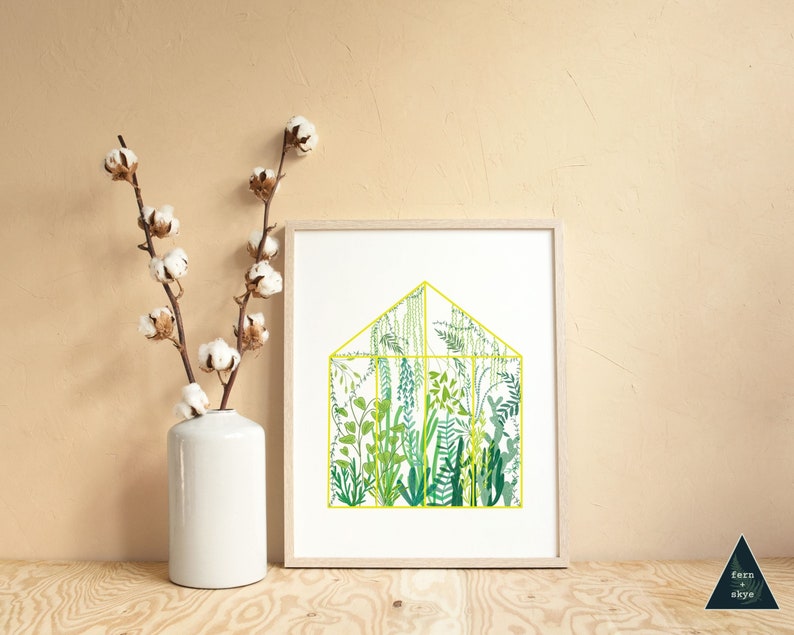 May include: A framed print of a yellow-outlined greenhouse filled with various green plants and ferns. The print is on a white background and is displayed on a light wood surface.