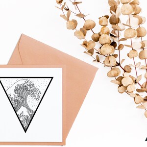 May include: A square greeting card with a black and white wave design inside a black triangle. The card is placed in a peach envelope. Dried eucalyptus branches are in the background. The card has the words "fern + skye" in the bottom right corner.