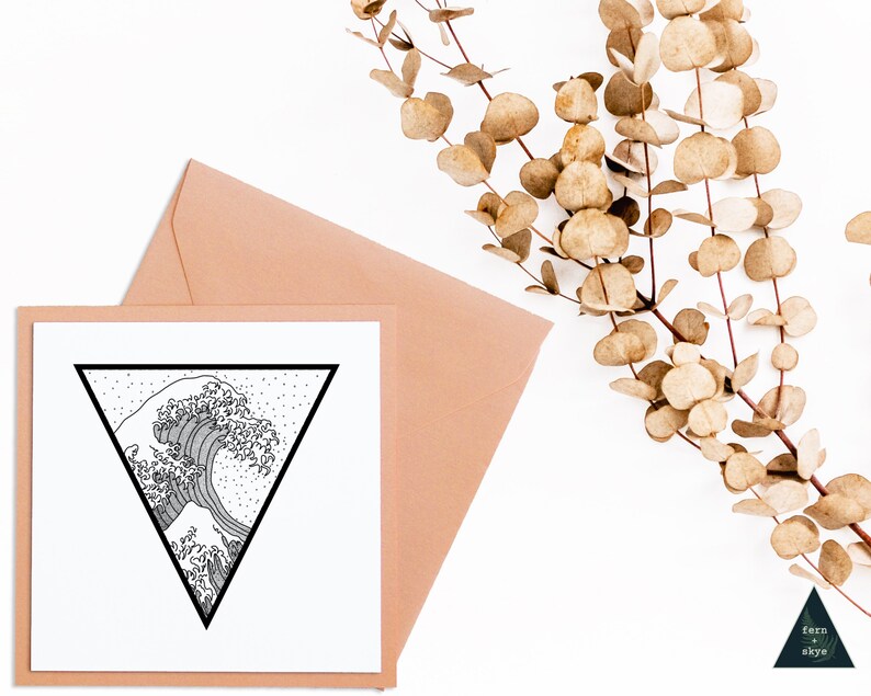 May include: A square greeting card with a black and white wave design inside a black triangle. The card is placed in a peach envelope. Dried eucalyptus branches are in the background. The card has the words "fern + skye" in the bottom right corner.