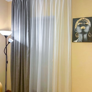 May include: Gray and white curtains hanging in a window. The curtains are lined up next to each other. The gray curtains are on the left and the white curtains are on the right.