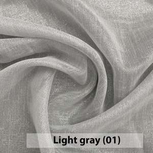 May include: Close-up of a light gray sheer fabric with a subtle shimmer. The fabric is draped and folded, showcasing its texture and drape.