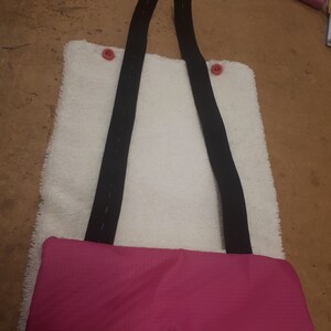 May include: A white, fluffy, rectangular pouch with two black straps and pink buttons. The pouch has a pink fabric lining.