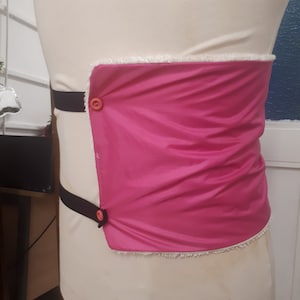 May include: A pink fabric belt with a white trim and two black straps with orange buttons.