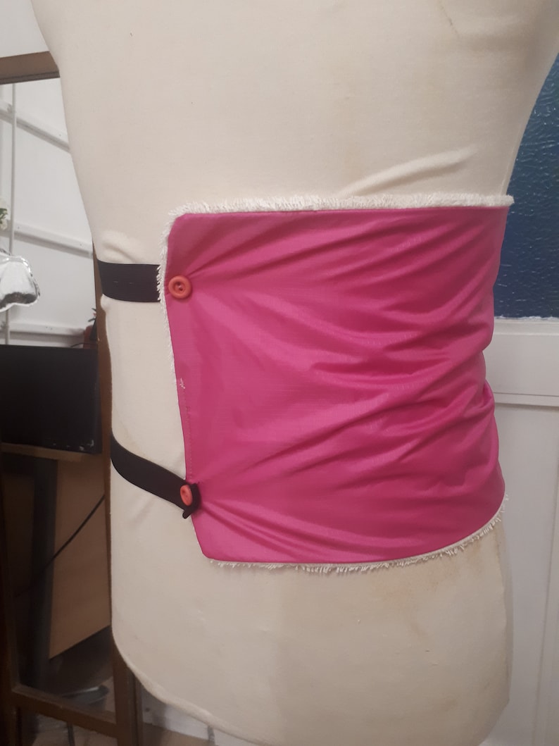 May include: A pink fabric belt with a white trim and two black straps with orange buttons.
