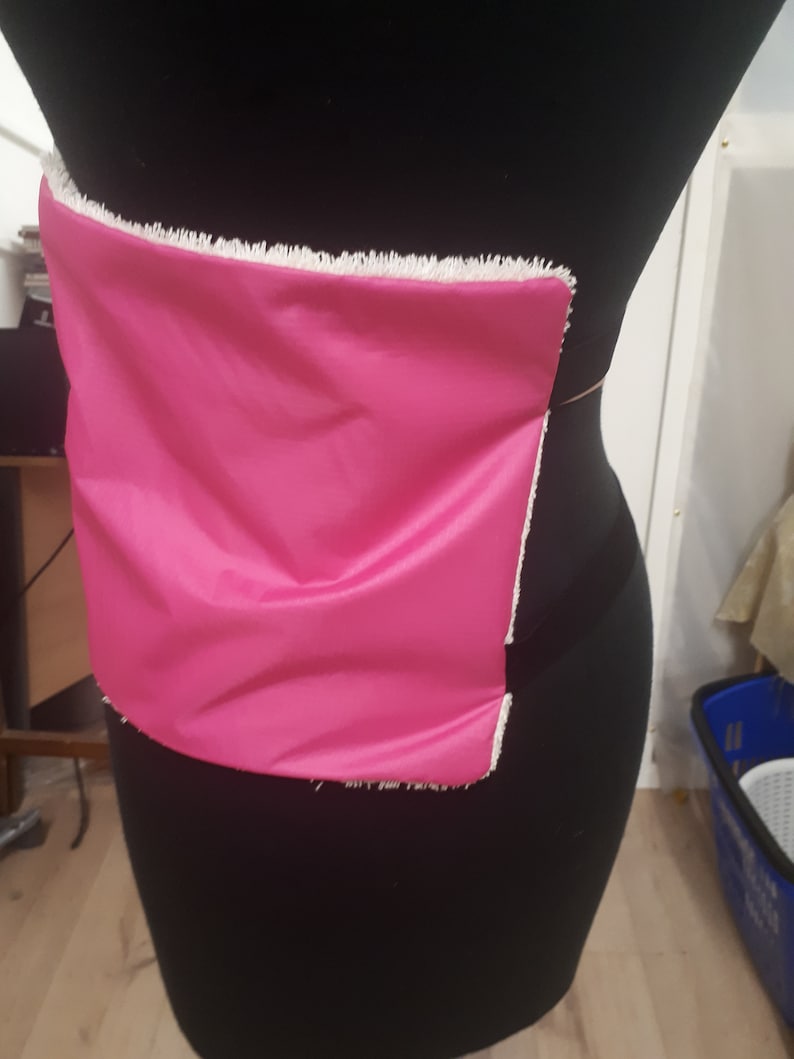 May include: A pink fabric panel with a white frayed edge is attached to a black dress form.