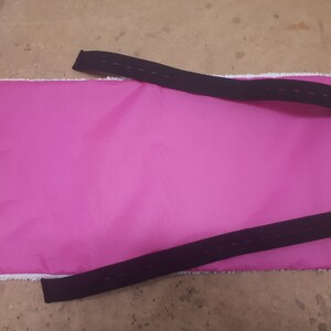 May include: Pink fabric mat with two black adjustable straps and two pink buttons.