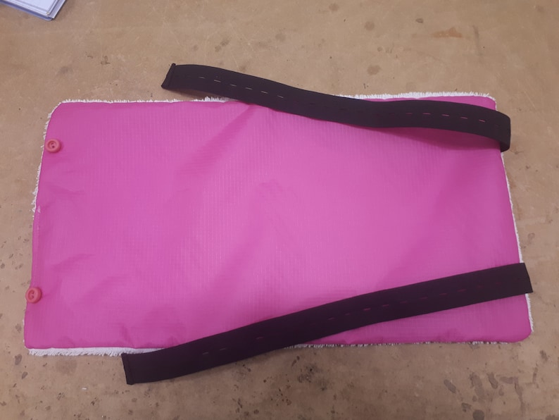 May include: Pink fabric mat with two black adjustable straps and two pink buttons.