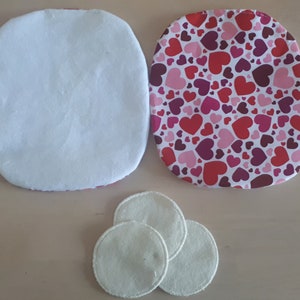 Peut inclure: Trois disques de coton blanc et deux morceaux de tissu de forme ovale. Un morceau de tissu est blanc et l'autre est blanc avec un motif de cœurs roses et rouges.