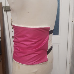 May include: A pink fabric panel with white trim and black straps. The panel is attached to a white form.