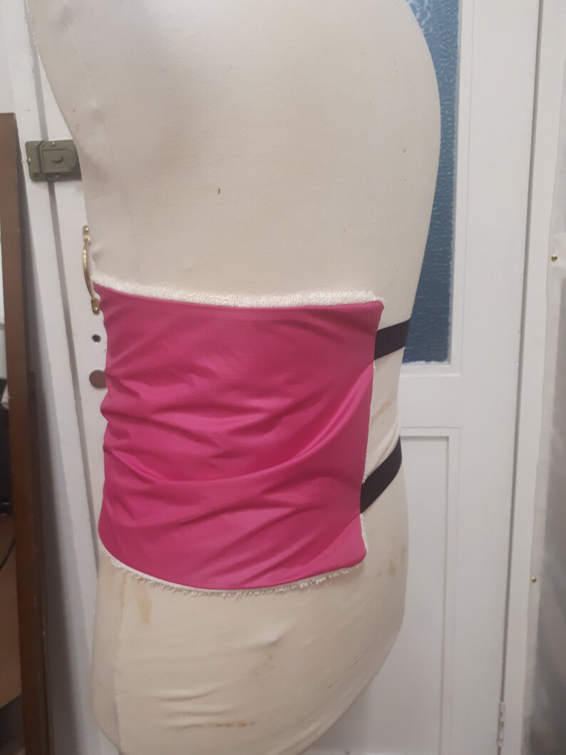 May include: A pink fabric panel with white trim and black straps. The panel is attached to a white form.