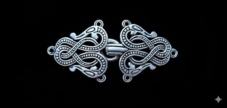 May include: Silver-toned metal clasp with an intricate, intertwined design. The clasp features two stylized dragon heads and a central bar for closure. The design is symmetrical and detailed, set against a black background.