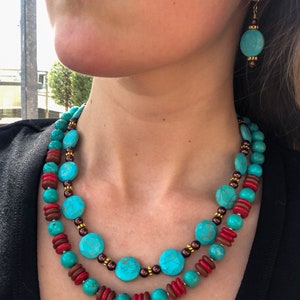 May include: Turquoise and red beaded necklace and matching earrings. The necklace features large turquoise-colored round beads, interspersed with smaller red and brown beads. The earrings have a similar design, with turquoise beads and gold-colored accents.