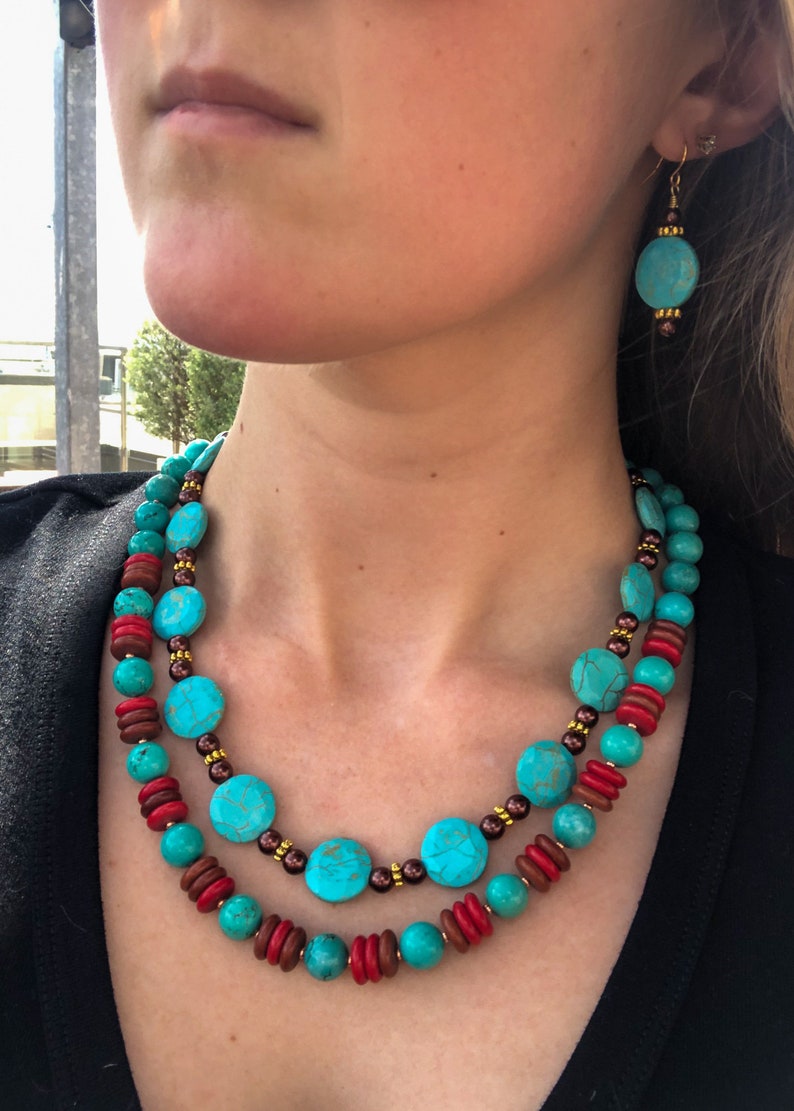 May include: Turquoise and red beaded necklace and matching earrings. The necklace features large turquoise-colored round beads, interspersed with smaller red and brown beads. The earrings have a similar design, with turquoise beads and gold-colored accents.
