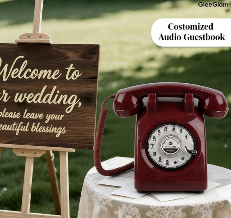 May include: A burgundy rotary dial telephone sits on a lace-covered table. The phone is connected by a coiled cord. A wooden sign with the words "Welcome to our wedding" is in the background. The text "Costomized Audio Guestbook" is also visible.