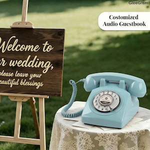 May include: A light blue vintage telephone with a rotary dial sits on a lace-covered table. The phone is a classic design, with a curved handset and a coiled cord. The text "Costomized Audio Guestbook" is visible.
