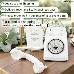 May include: A white vintage rotary phone with a matching handset rests on a wooden surface. The phone features a circular dial with numbers and the word "GREETING". A wedding invitation is behind the phone. The image also includes text about logistics.