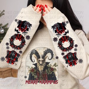 May include: A cream-colored sweatshirt with a festive Christmas design featuring a horned figure with a beard and the text "Merry Krampus". The sleeves have a repeating pattern of wreaths, candles, and snowflakes.