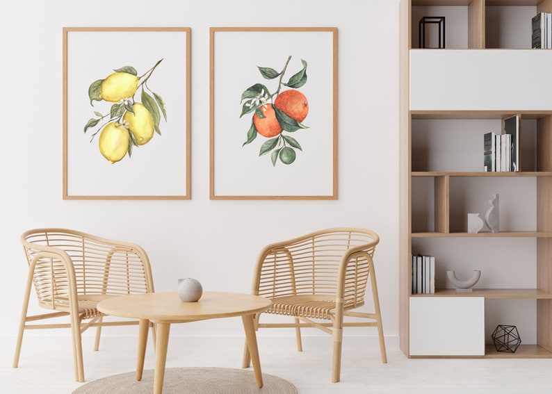 May include: Two framed watercolor paintings of citrus fruit branches. The left painting shows a lemon branch with three lemons. The right painting shows an orange branch with two oranges and a lime.